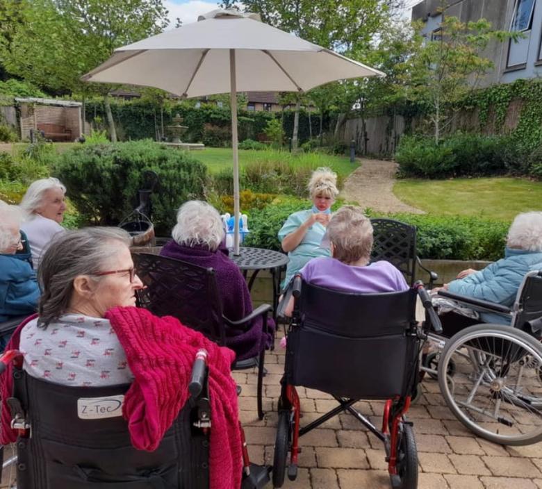 care home residents sat outside in the garden with nurse telling them a story