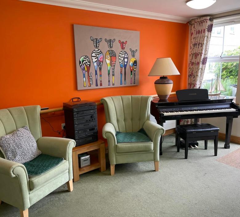 room in nursing home with arm chairs and a piano with a bright orange feature wall