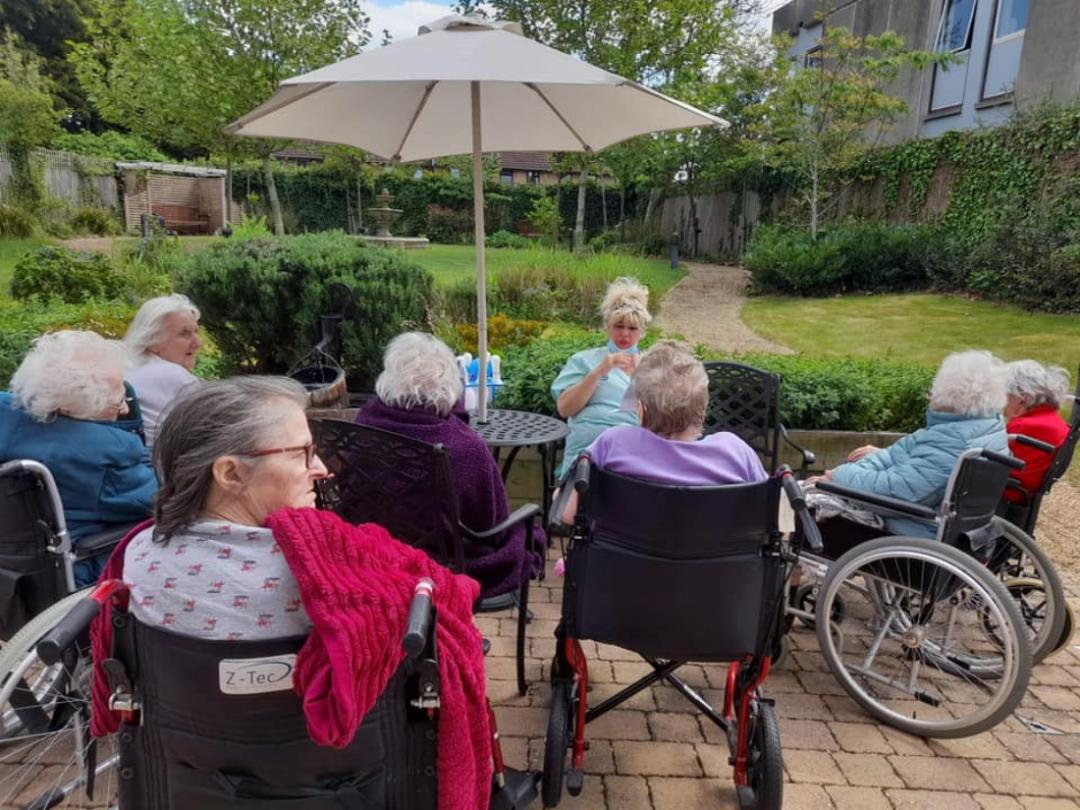 care home residents sat outside in the garden with nurse telling them a story