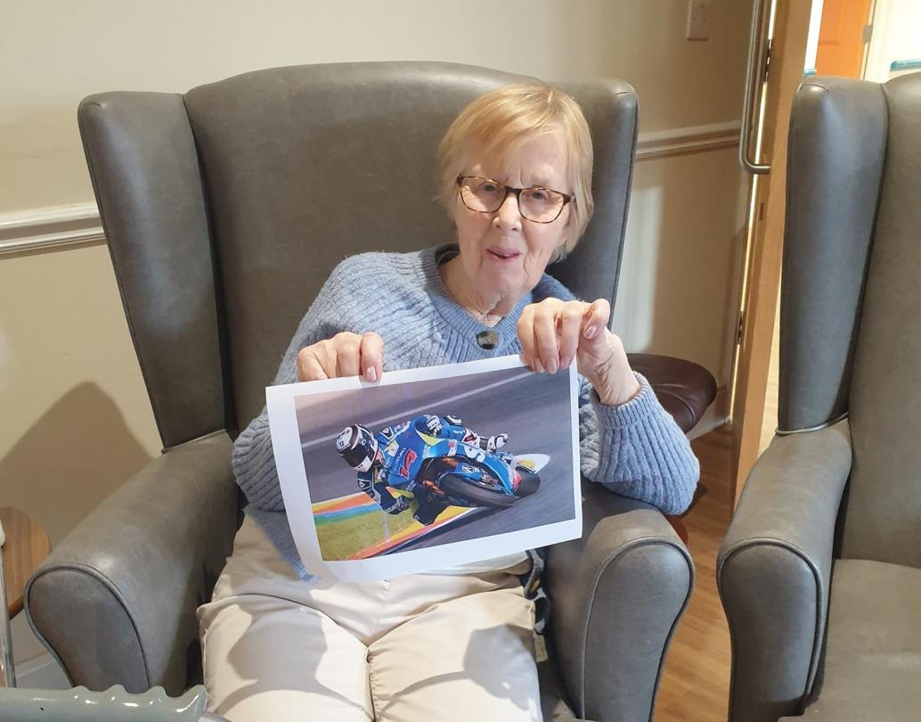 care home resident smiling holding up printed out image of a motorcyclist racing
