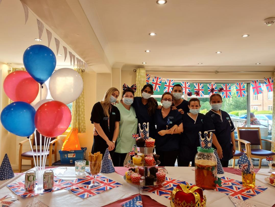 nursing home team with masks posing in front of a table full of party food and balloons