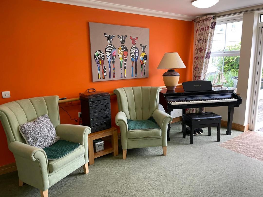room in nursing home with arm chairs and a piano with a bright orange feature wall