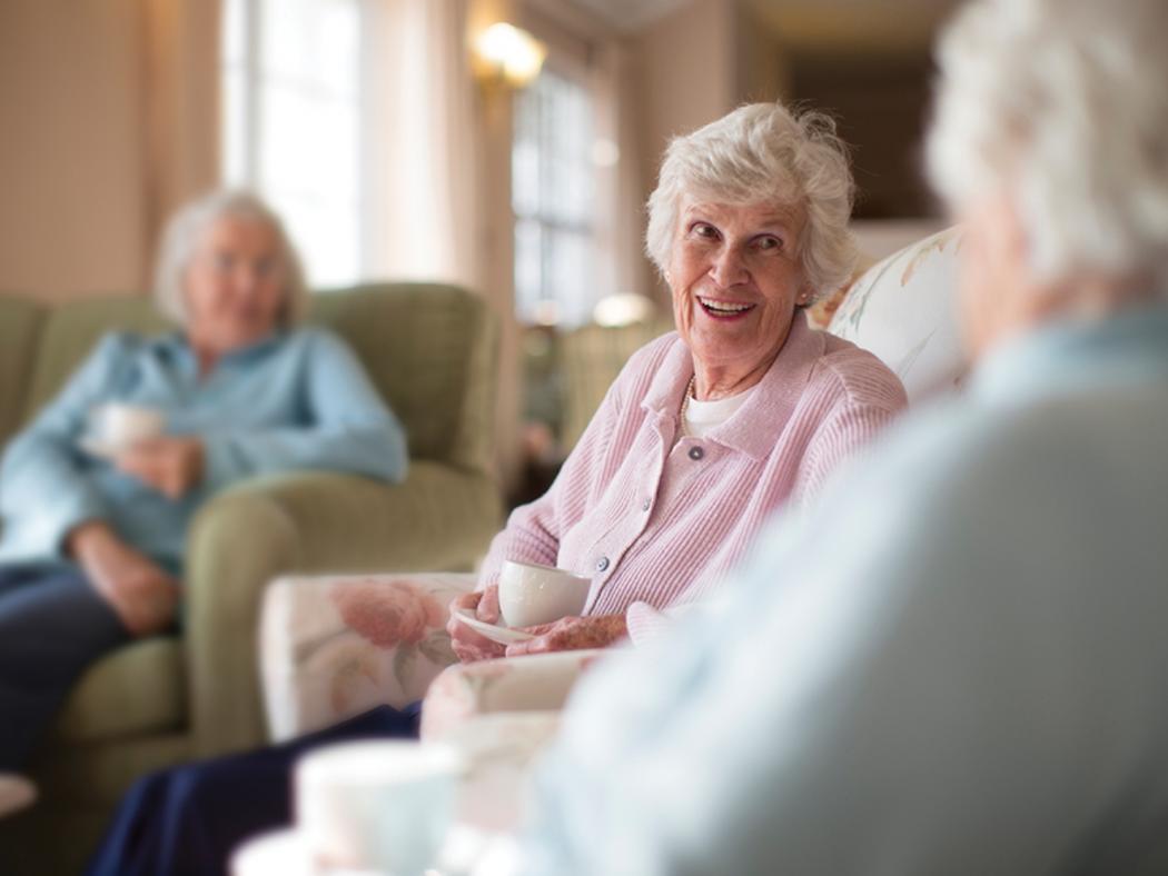 elderly care home residents sat in chairs talking and smiling