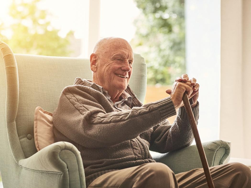 elderly man sitting in chair smiling resting on walking stick in a care home