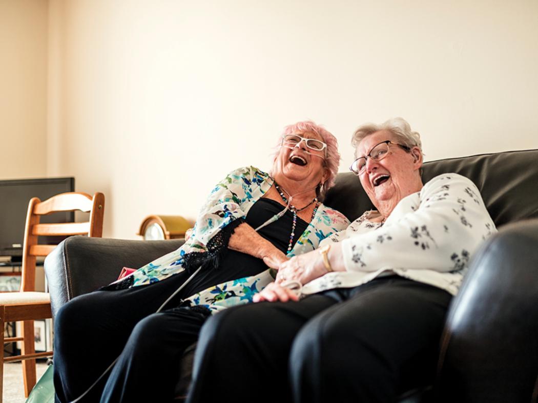 two elderly ladies sat on a sofa laughing together 