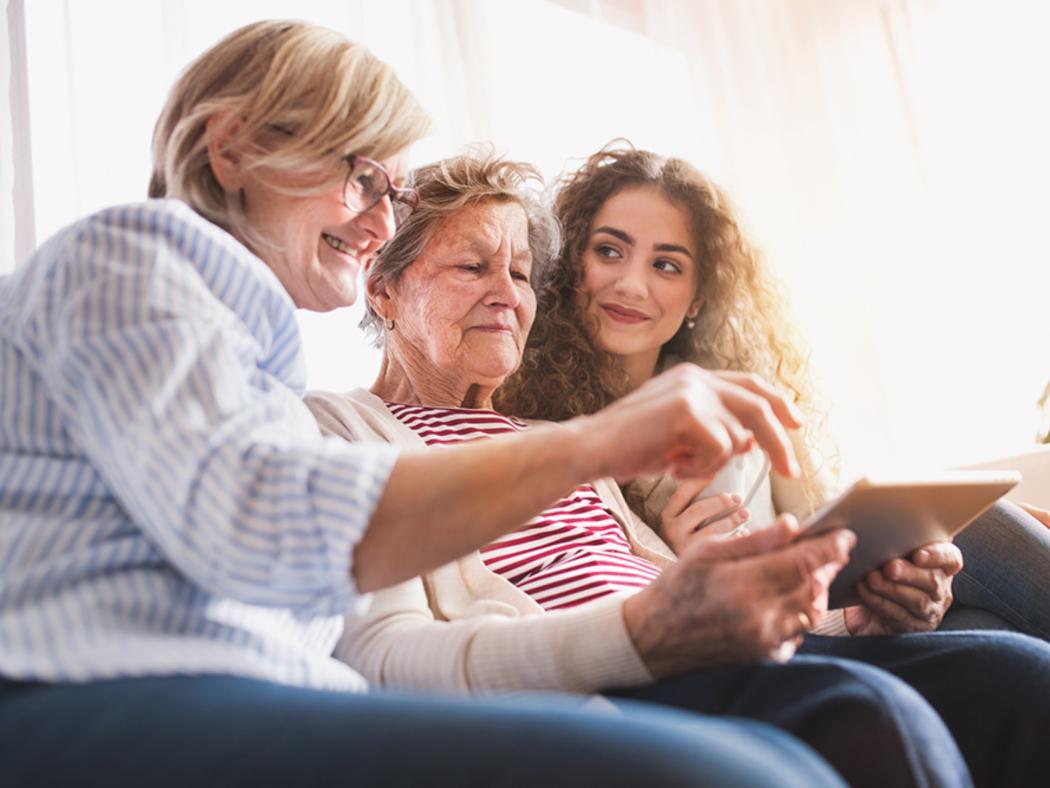 elderly lady looking at tablet with younger woman and younger girl either side of her laughing