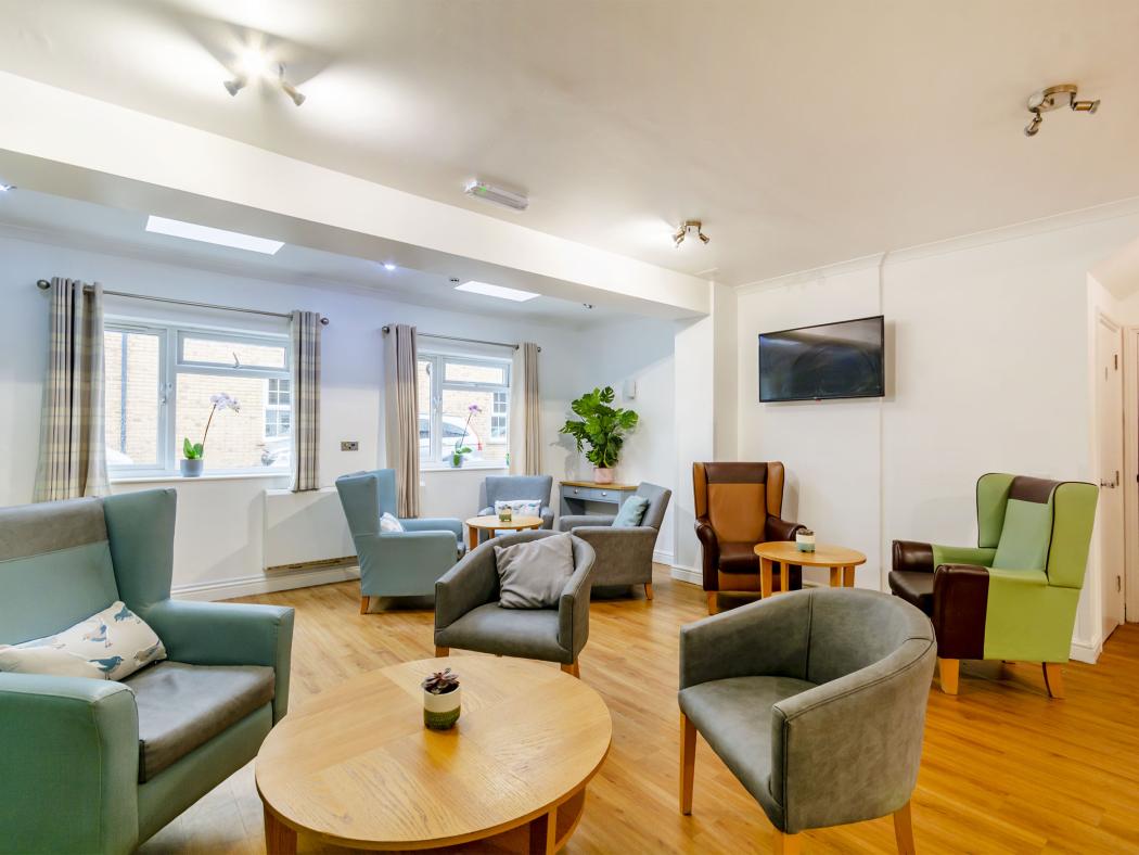 A bright, spacious lounge featuring comfortable chairs, a television, and large windows with natural light streaming in