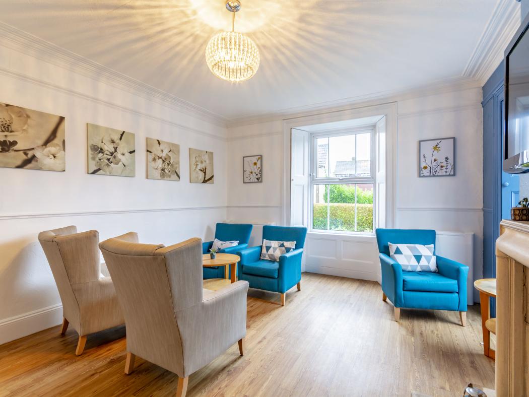 Image of a bright lounge at The Grove Residential Home with blue armchairs and floral artwork on the walls