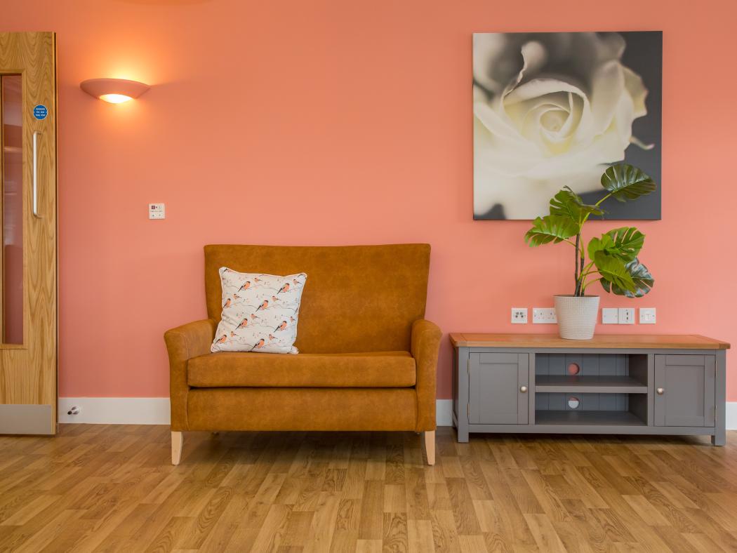 Comfortable seating area in a cosy room at Rose Garden Care Home, featuring a flower painting and soft, warm decor