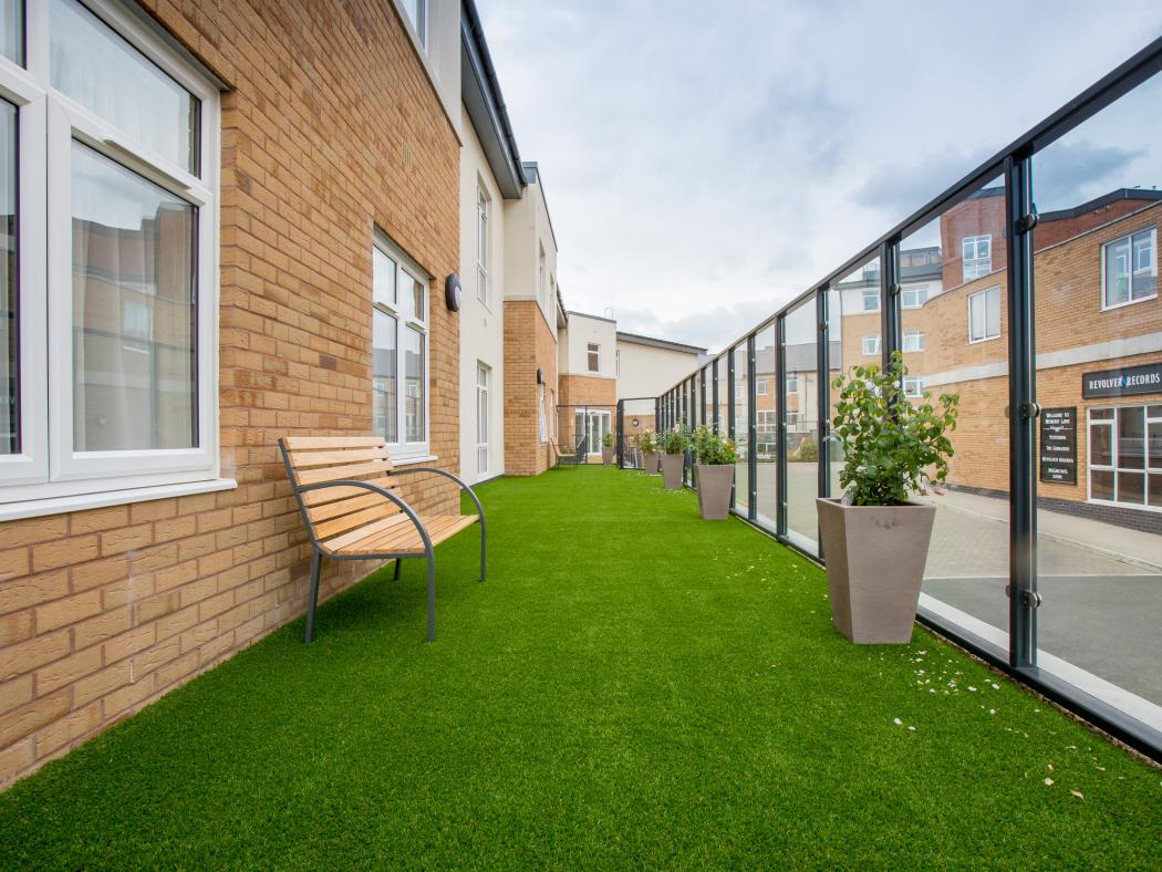 Outdoor artificial grass area with seating bench along the side of Rose Garden Care Home