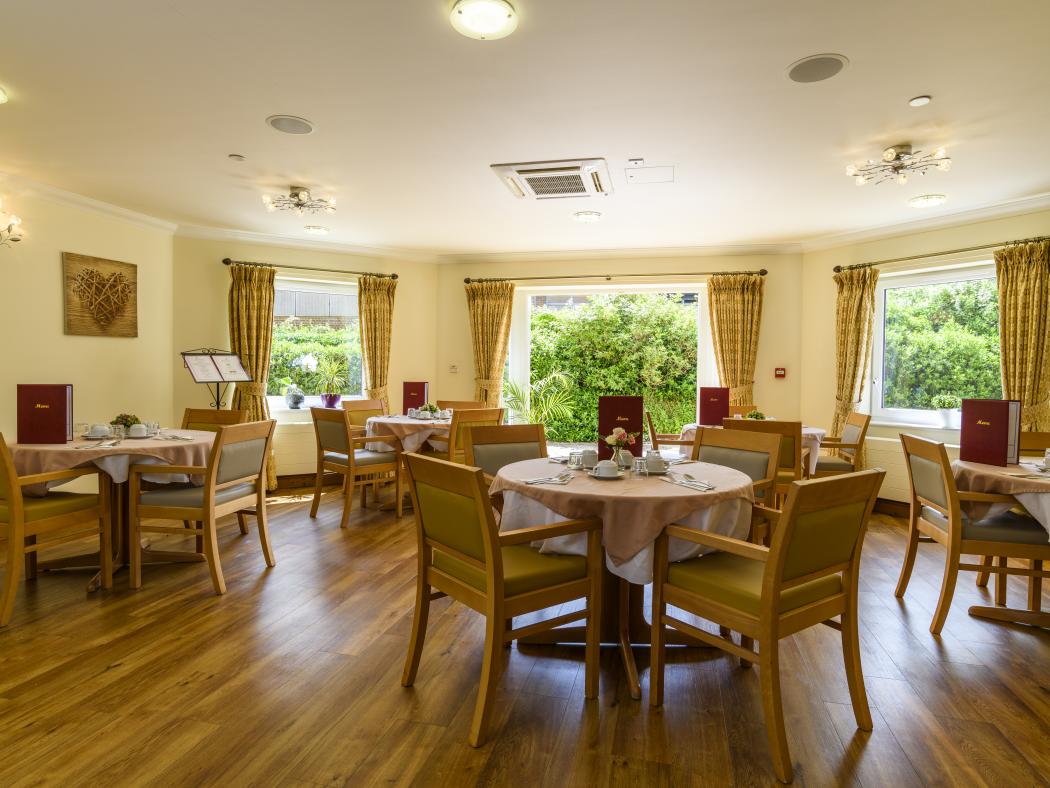 care home dining room with tables and chairs laid and light streaming in through windows