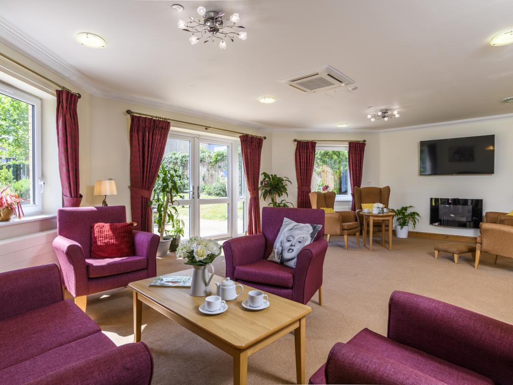 living room in care home with armchairs, sofas, tables and a large tv on the wall