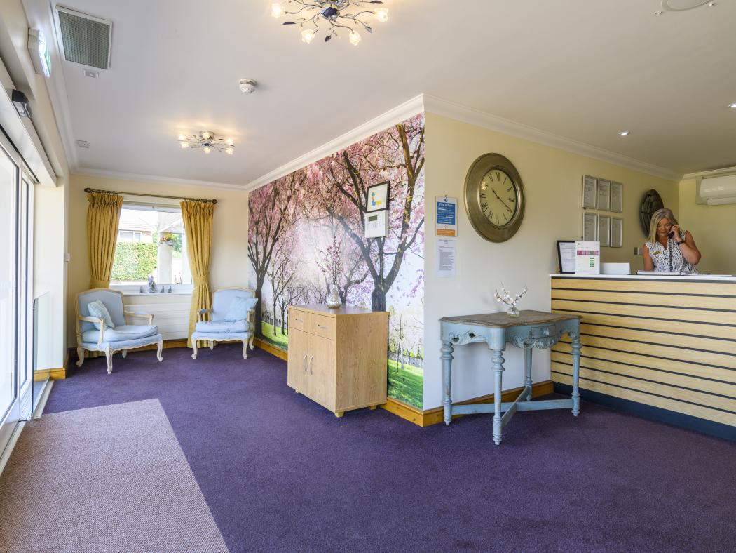 Care home lobby with seats and a receptionist at the desk on the phone