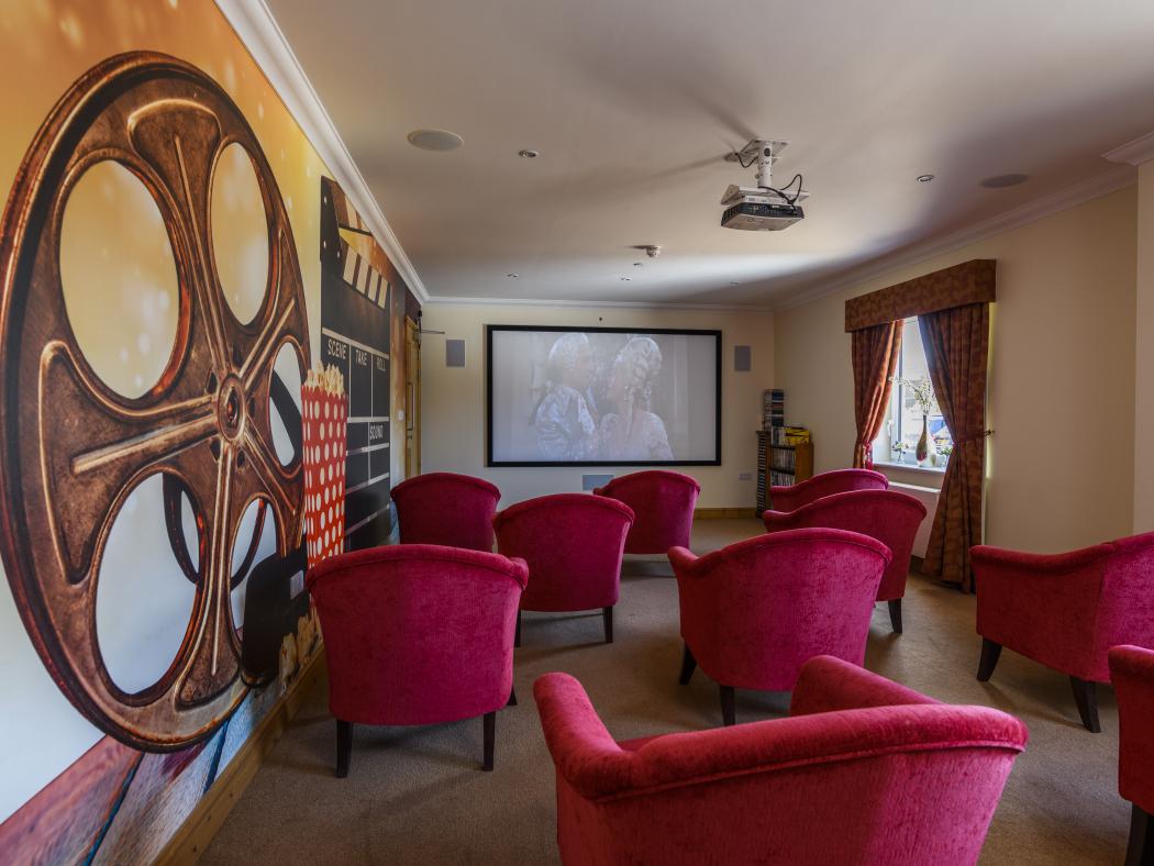 care home theatre room with projector and plush red armchairs facing it
