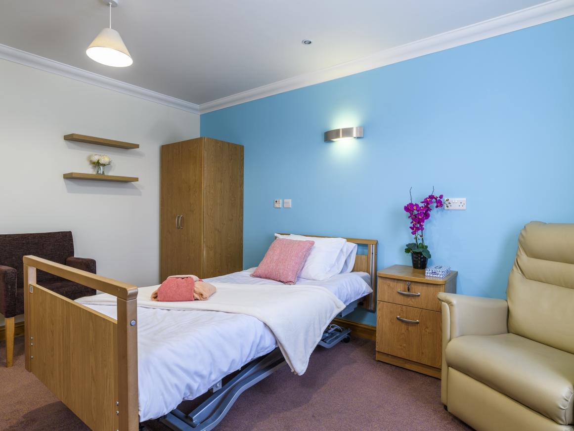 Care home bedroom with blue feature wall and wooden furniture