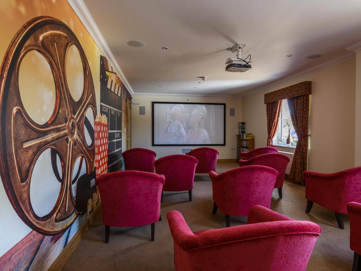 care home theatre room with projector and plush red armchairs 