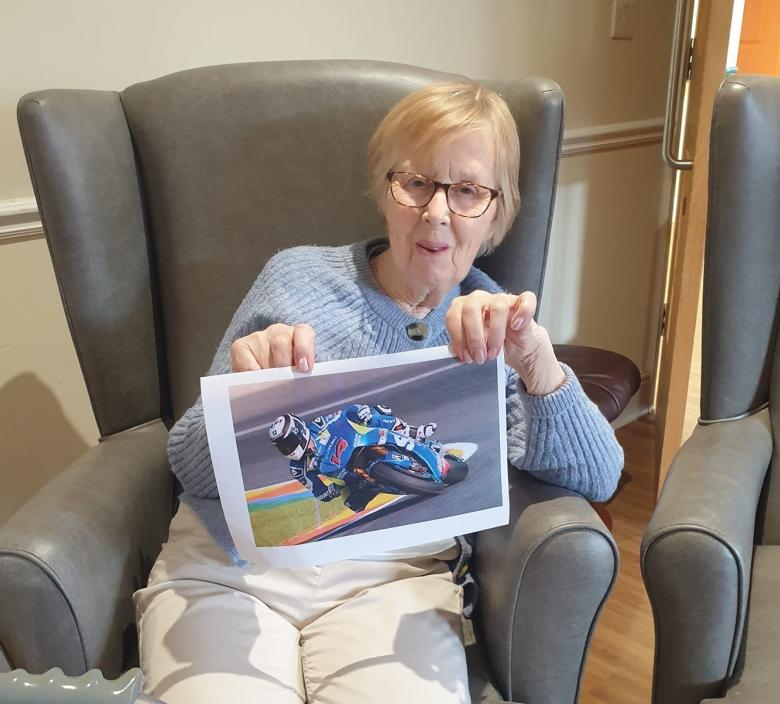 care home resident smiling holding up printed out image of a motorcyclist racing