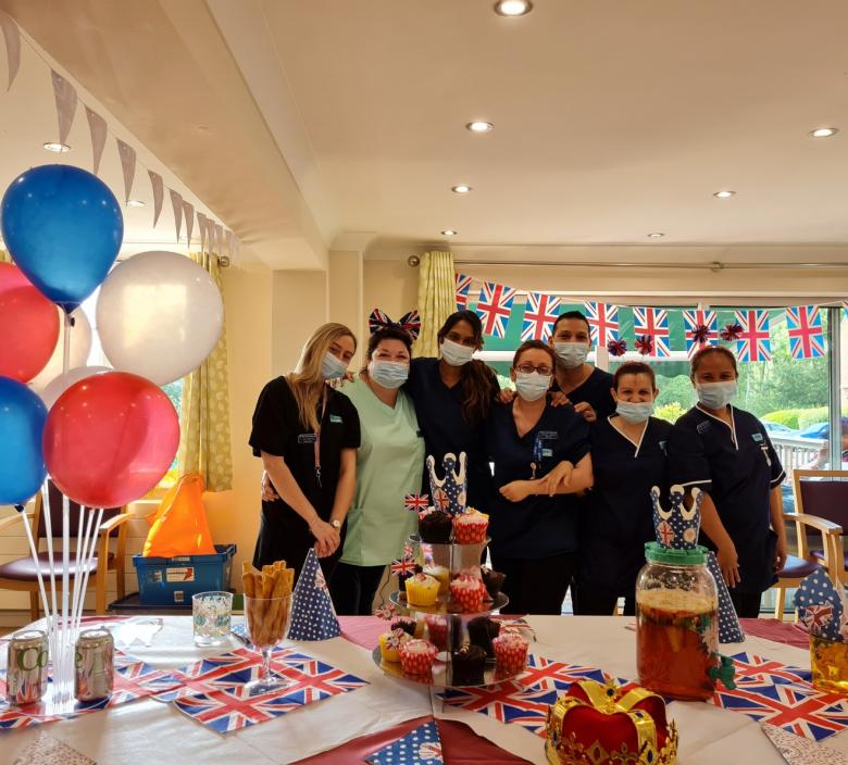 nursing home team with masks posing in front of a table full of party food and balloons